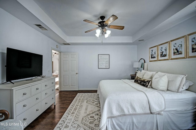 bedroom featuring ceiling fan, a raised ceiling, dark wood-type flooring, and connected bathroom