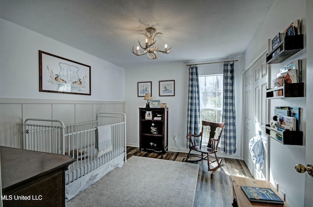 bedroom with a closet, a textured ceiling, a nursery area, dark hardwood / wood-style flooring, and a chandelier