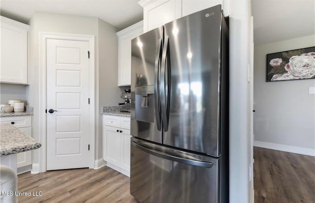 14451 Quail Ridge Dr, Gulfport, MS 39503 - kitchen with stainless steel refrigerator with ice dispenser, wood finished floors, white cabinets, baseboards, and light stone countertops