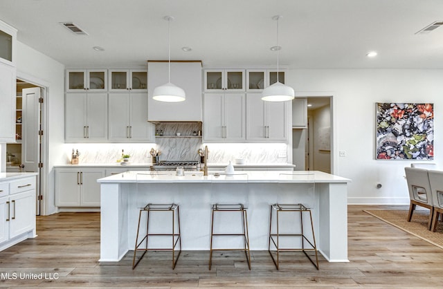 kitchen featuring white cabinetry, hanging light fixtures, a breakfast bar, and a center island with sink