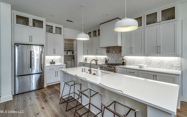 kitchen with appliances with stainless steel finishes, a kitchen bar, decorative backsplash, hanging light fixtures, and a kitchen island with sink