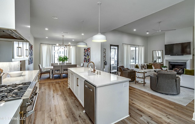 kitchen with sink, hanging light fixtures, stainless steel appliances, extractor fan, and an island with sink