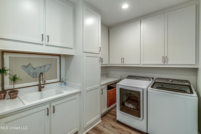 laundry area featuring washer and dryer, sink, light hardwood / wood-style floors, and cabinets