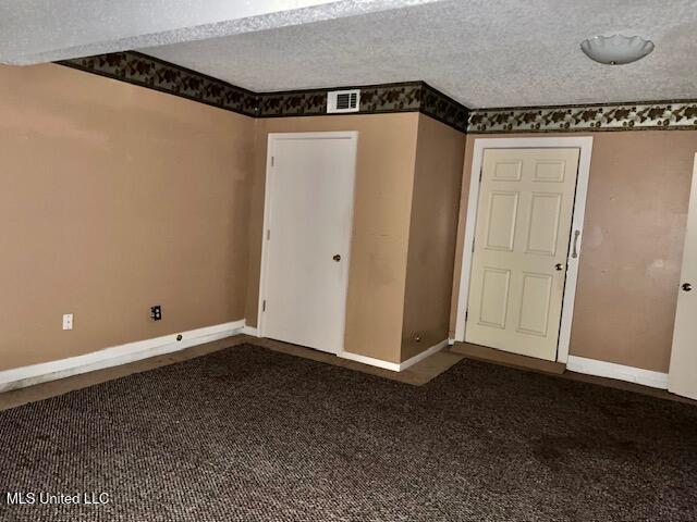 spare room featuring a textured ceiling and dark colored carpet