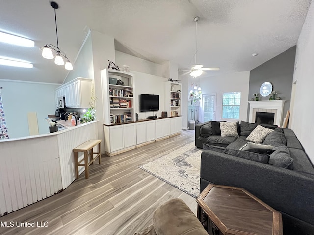 9929 Kahana St, Diamondhead, MS 39525 - living room featuring vaulted ceiling, light wood finished floors, ceiling fan, a tiled fireplace, and a textured ceiling