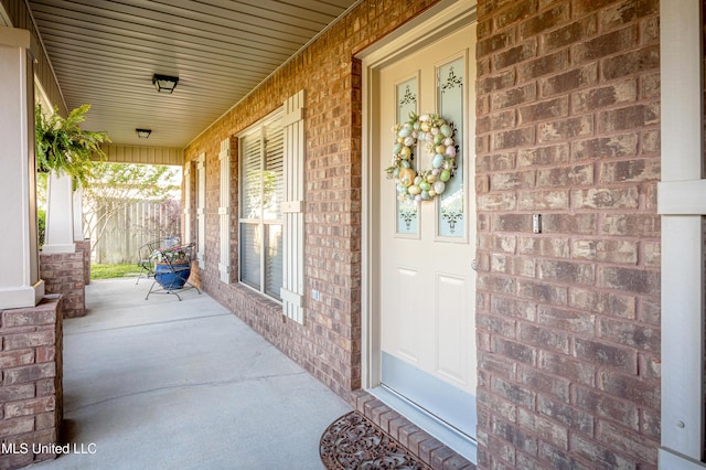 view of exterior entry with brick siding and covered porch