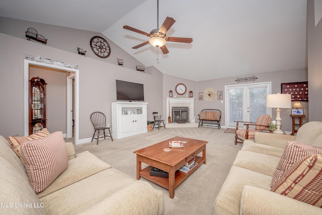 living room with baseboards, a ceiling fan, high vaulted ceiling, a glass covered fireplace, and light carpet