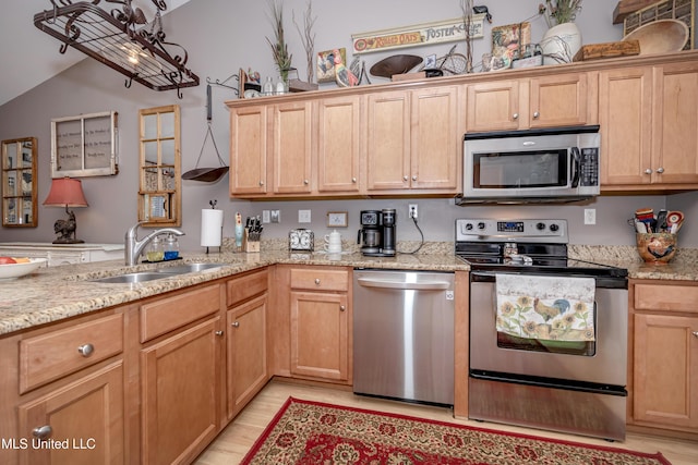 kitchen featuring stainless steel appliances, light stone countertops, light wood-style floors, and a sink