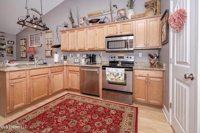 kitchen with a peninsula, vaulted ceiling, light stone counters, stainless steel appliances, and light wood finished floors