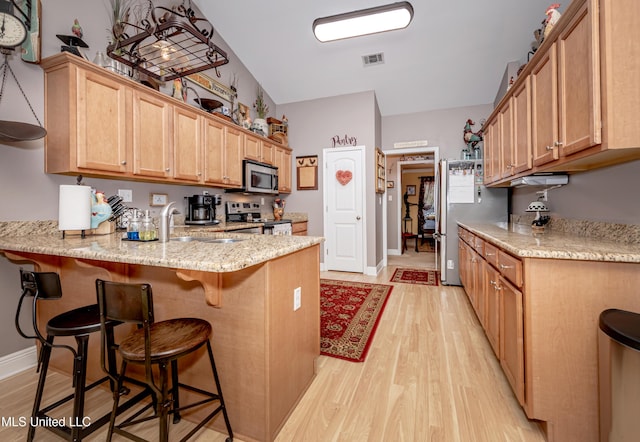 kitchen featuring a sink, light wood-type flooring, appliances with stainless steel finishes, a kitchen bar, and a peninsula