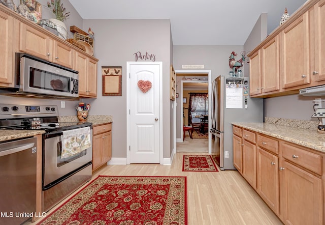 kitchen featuring light wood-style floors, light stone countertops, stainless steel appliances, light brown cabinets, and baseboards