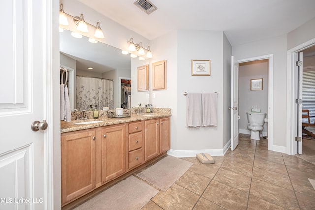 bathroom featuring visible vents, toilet, a sink, double vanity, and baseboards