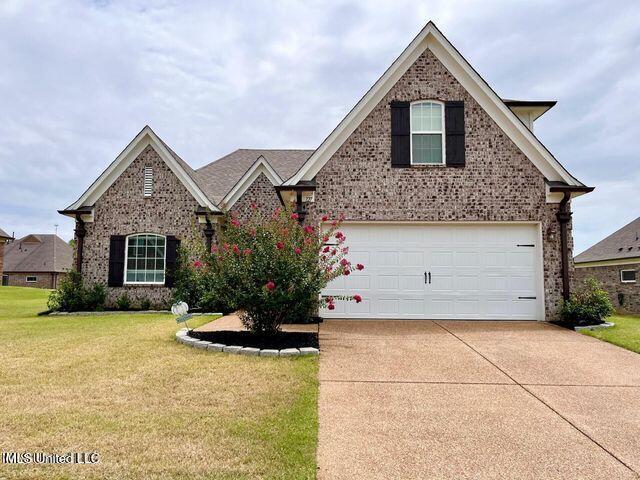 traditional-style house with a garage, concrete driveway, a front lawn, and brick siding