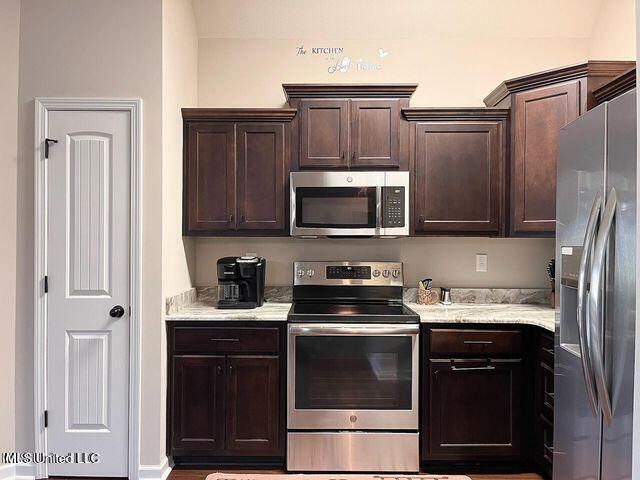 kitchen with stainless steel appliances, light stone counters, and dark brown cabinets