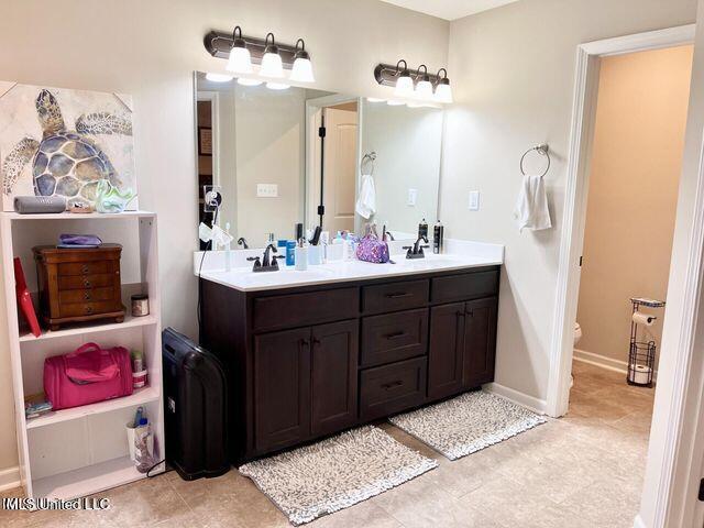 full bathroom with toilet, a sink, baseboards, and double vanity