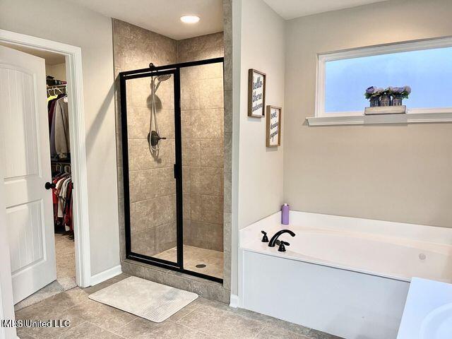 bathroom featuring a shower stall, baseboards, a walk in closet, and a bath