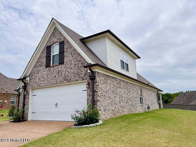 view of side of property with concrete driveway, brick siding, a yard, and an attached garage