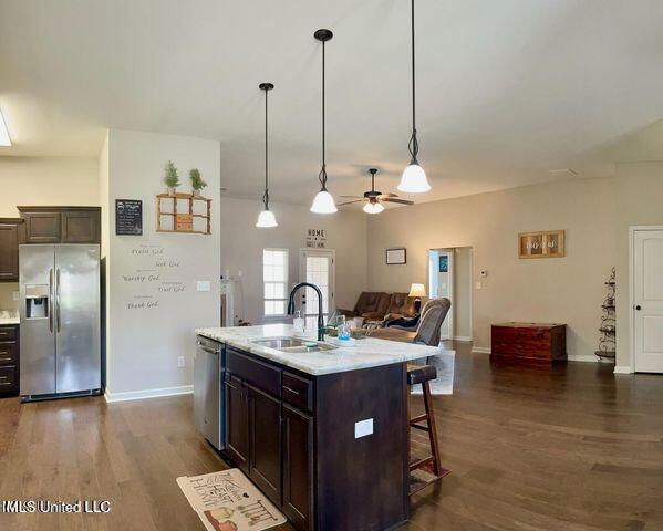 kitchen featuring a sink, a kitchen breakfast bar, open floor plan, dark brown cabinets, and appliances with stainless steel finishes