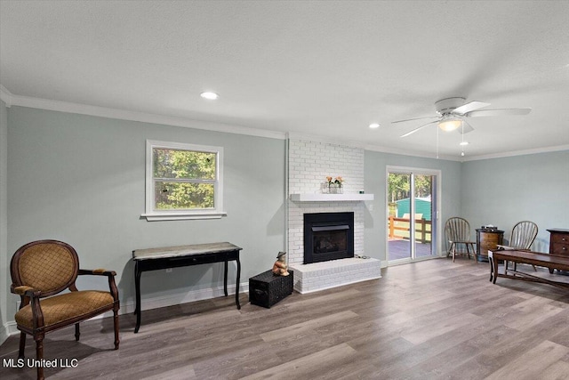 living area with light wood-type flooring, a textured ceiling, a brick fireplace, ceiling fan, and ornamental molding