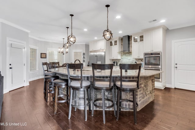kitchen with wall chimney exhaust hood, stainless steel appliances, ornamental molding, a spacious island, and backsplash