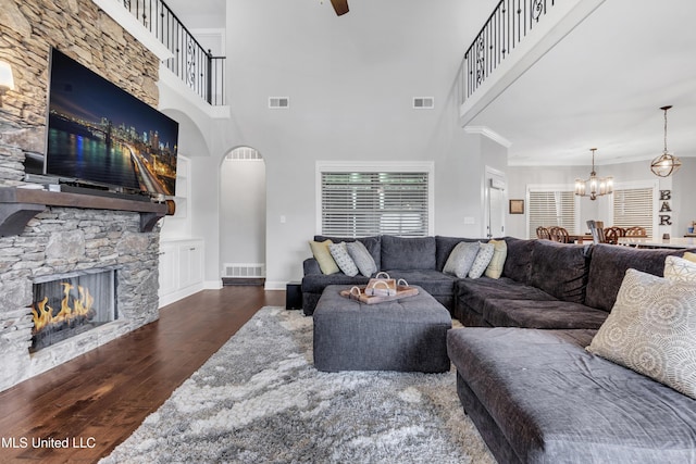living area with hardwood / wood-style flooring, a fireplace, a chandelier, arched walkways, and a towering ceiling