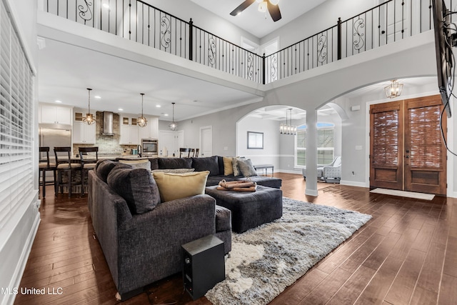 living area featuring arched walkways, ceiling fan, dark wood-style floors, a high ceiling, and a chandelier