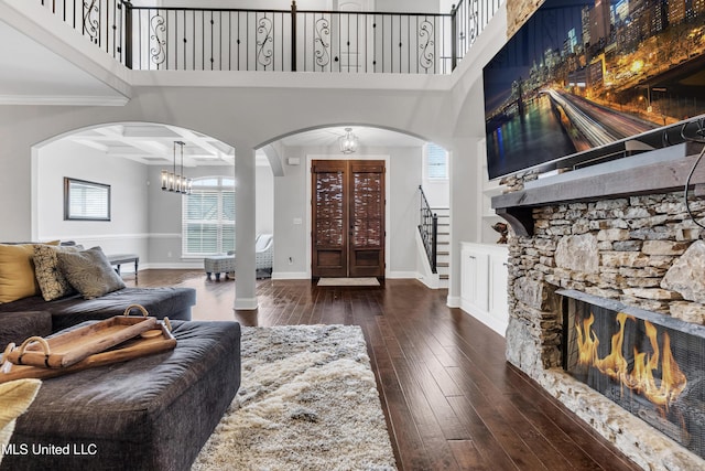 living room featuring stairway, a stone fireplace, arched walkways, wood-type flooring, and a chandelier