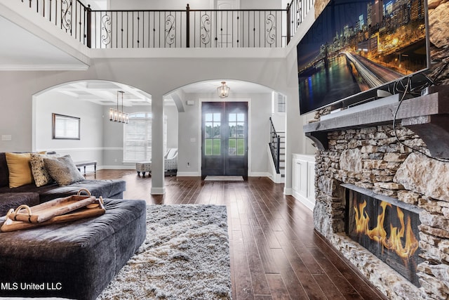 living area with arched walkways, wood-type flooring, plenty of natural light, stairs, and a towering ceiling