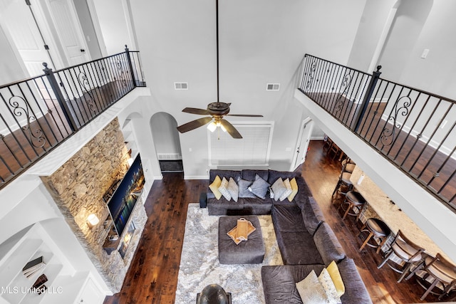 living room featuring ceiling fan, a towering ceiling, wood-type flooring, a premium fireplace, and baseboards