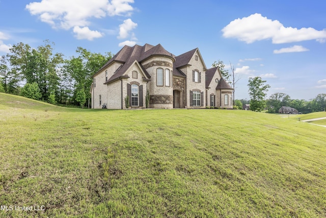 french country inspired facade with brick siding, a front yard, and stone siding