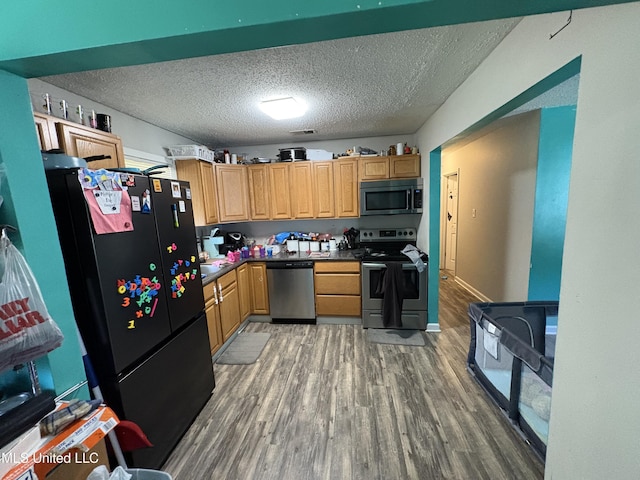 kitchen featuring dark countertops, a textured ceiling, stainless steel appliances, and wood finished floors