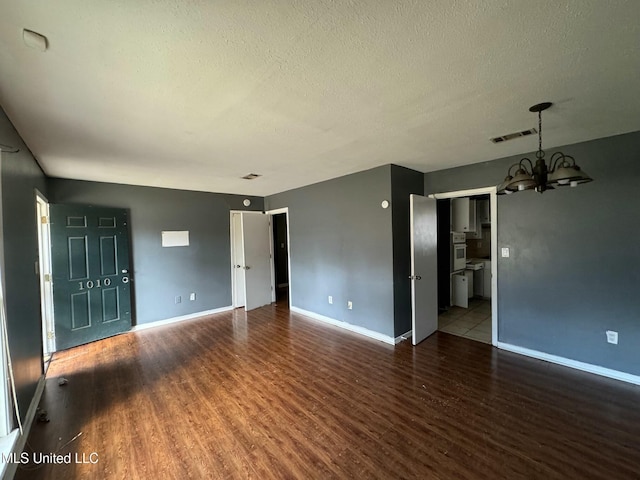 unfurnished living room featuring a textured ceiling, a notable chandelier, and dark hardwood / wood-style flooring