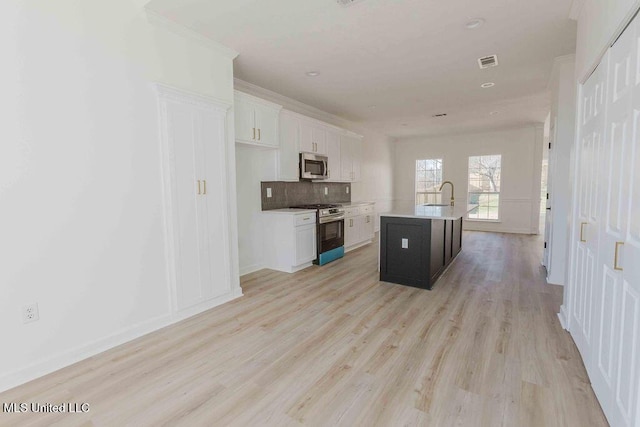 kitchen featuring a center island with sink, stainless steel appliances, light countertops, white cabinetry, and a sink