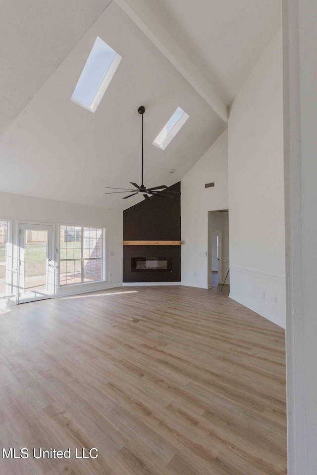 unfurnished living room with a skylight, a ceiling fan, light wood-style floors, beam ceiling, and a glass covered fireplace