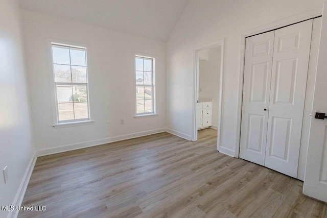 unfurnished bedroom with baseboards, vaulted ceiling, a closet, light wood finished floors, and ensuite bath