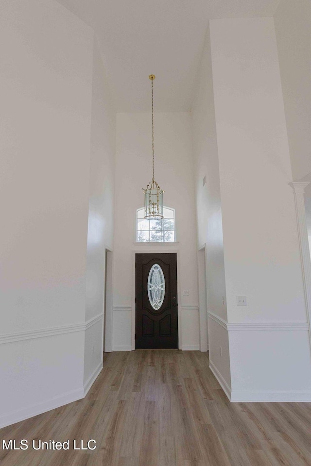 entrance foyer featuring baseboards, light wood finished floors, a towering ceiling, and an inviting chandelier