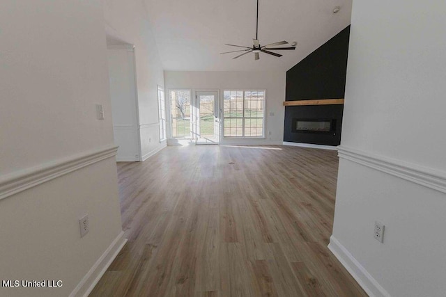 unfurnished living room featuring light wood-style flooring, a ceiling fan, a large fireplace, high vaulted ceiling, and baseboards