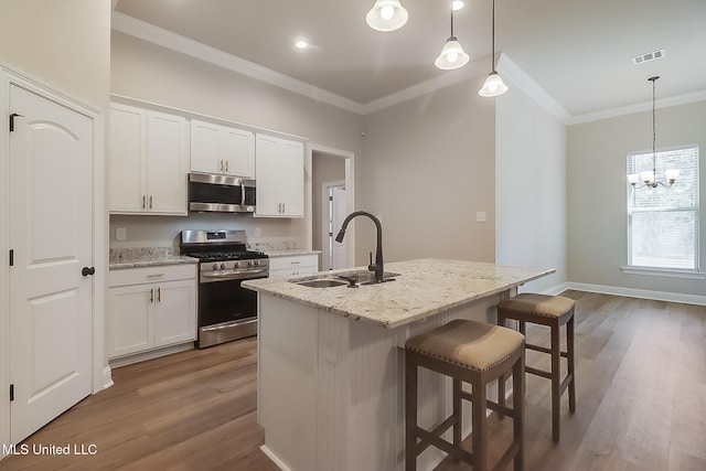 kitchen featuring decorative light fixtures, appliances with stainless steel finishes, a kitchen island with sink, and white cabinets