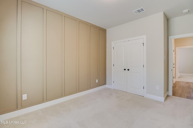 unfurnished bedroom with a closet, visible vents, light carpet, and baseboards