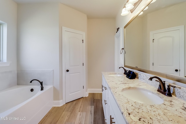 full bathroom featuring a garden tub, double vanity, wood finished floors, and a sink