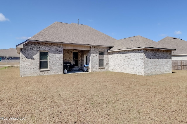 back of property with a patio area, a yard, brick siding, and roof with shingles