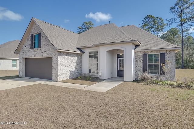 french country style house featuring brick siding, a front yard, concrete driveway, and roof with shingles