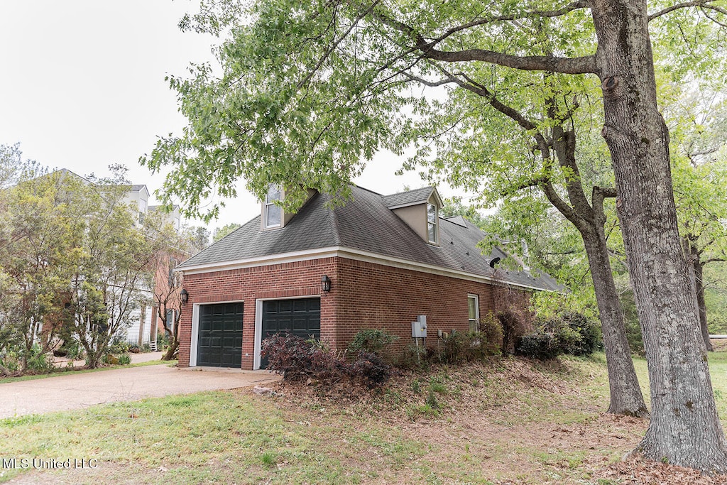view of side of home with concrete driveway, roof with shingles, brick siding, and a garage
