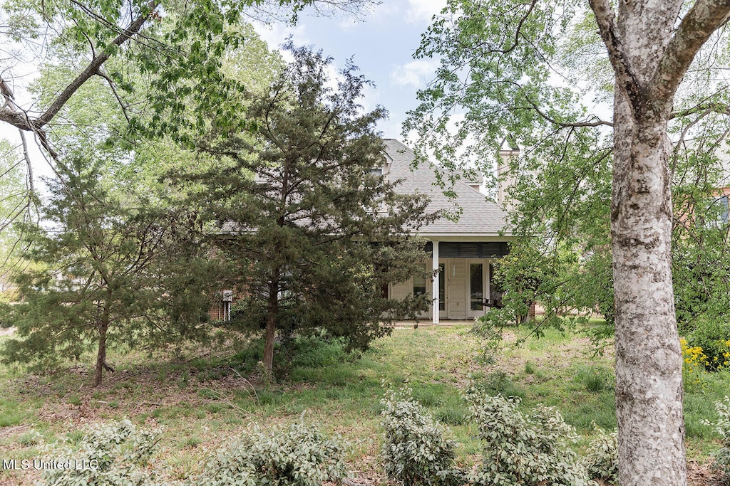 view of property hidden behind natural elements with roof with shingles and a chimney