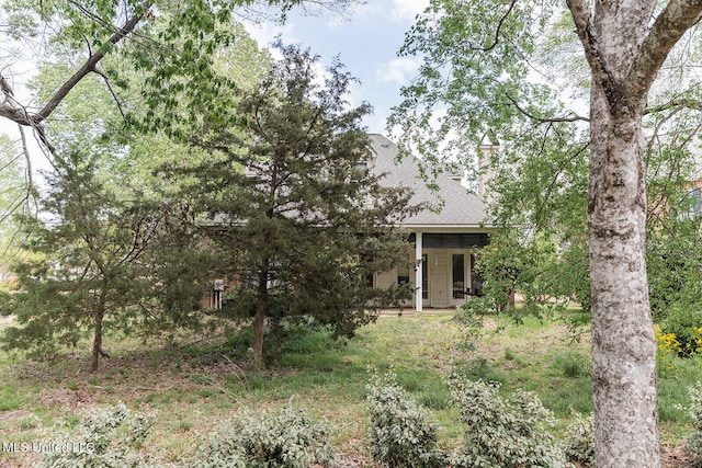 view of property hidden behind natural elements with roof with shingles and a chimney