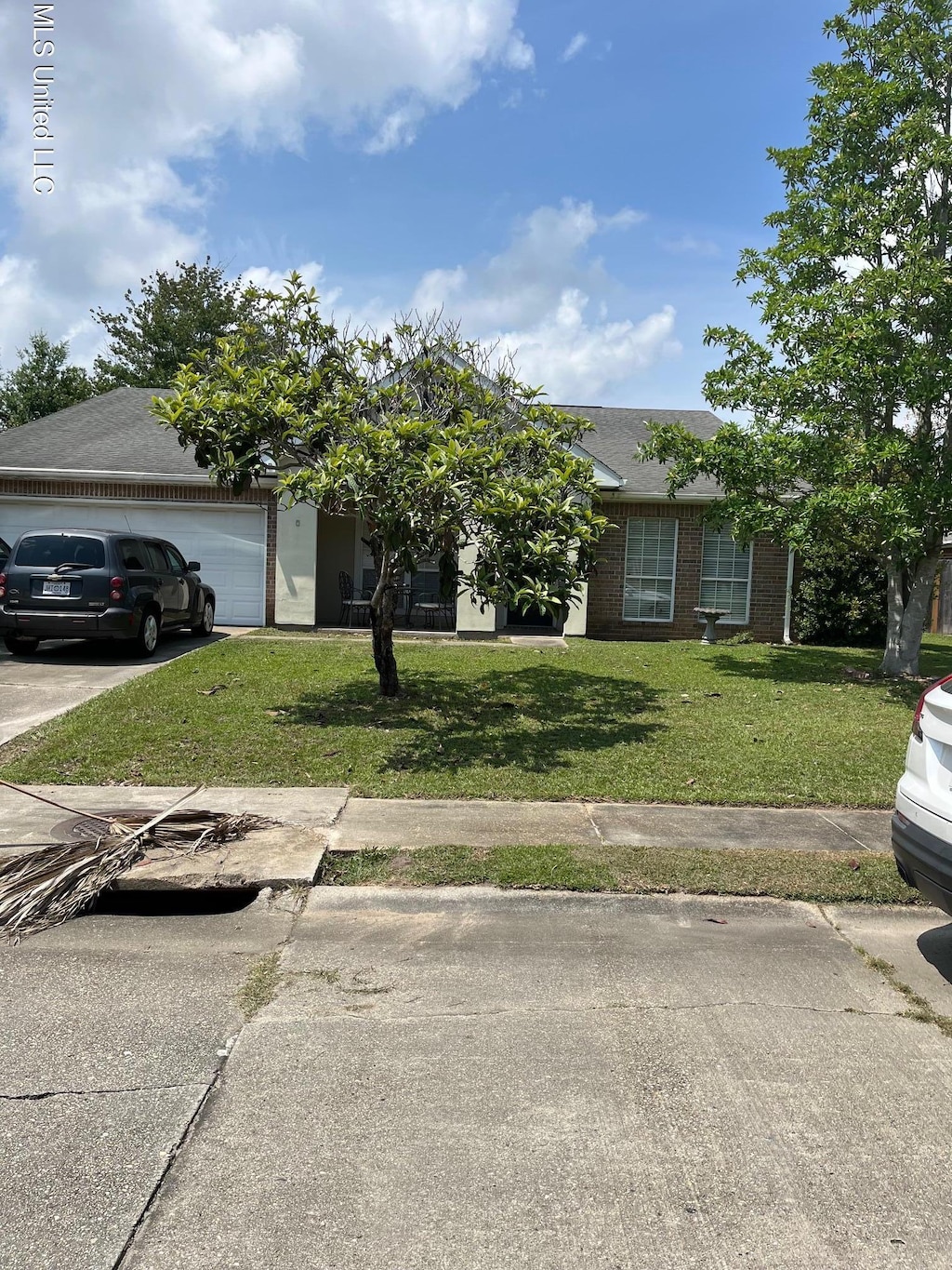 3603 Miles Ln, Ocean Springs, MS 39564 - view of property hidden behind natural elements featuring an attached garage, a front lawn, concrete driveway, brick siding, and a shingled roof