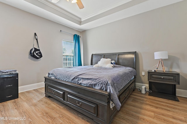 bedroom with light wood-style floors, a raised ceiling, ornamental molding, and baseboards