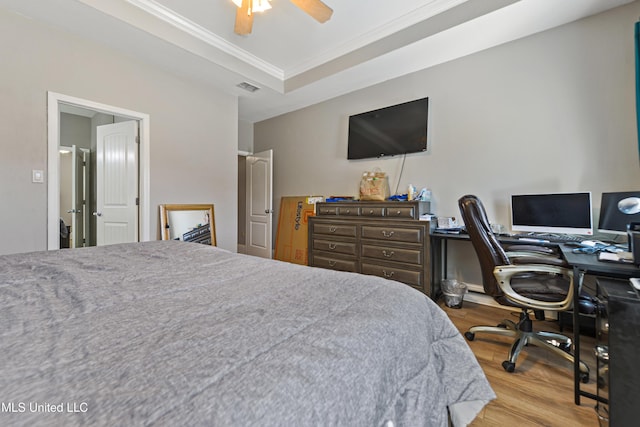 bedroom featuring a ceiling fan, visible vents, light wood finished floors, a raised ceiling, and crown molding