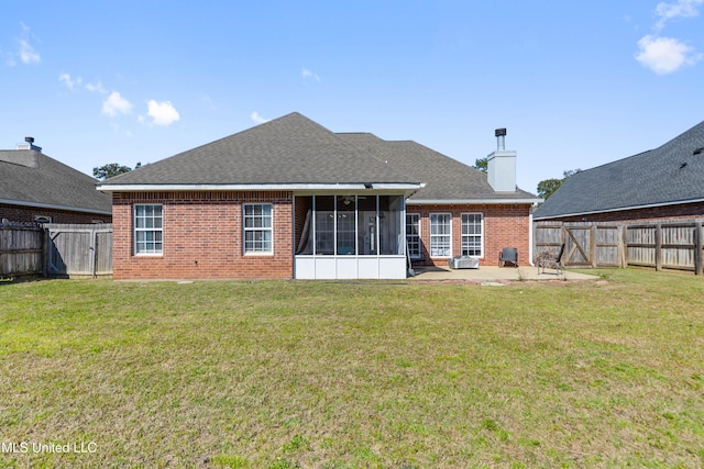 back of house featuring a sunroom, a fenced backyard, a yard, and brick siding