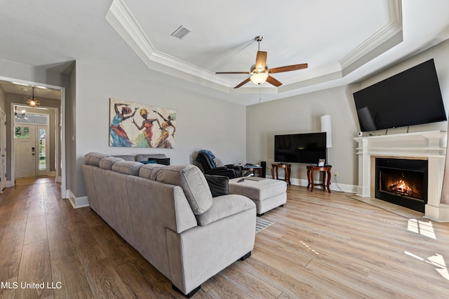 living area with a raised ceiling, visible vents, light wood-style flooring, and baseboards